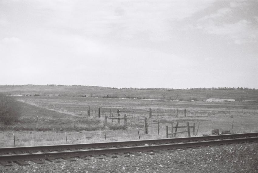 Black and white photo of a field with a train track in the foreground