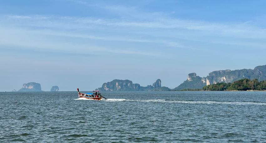 A long-tail boat traveling in the distance with mountains in the background