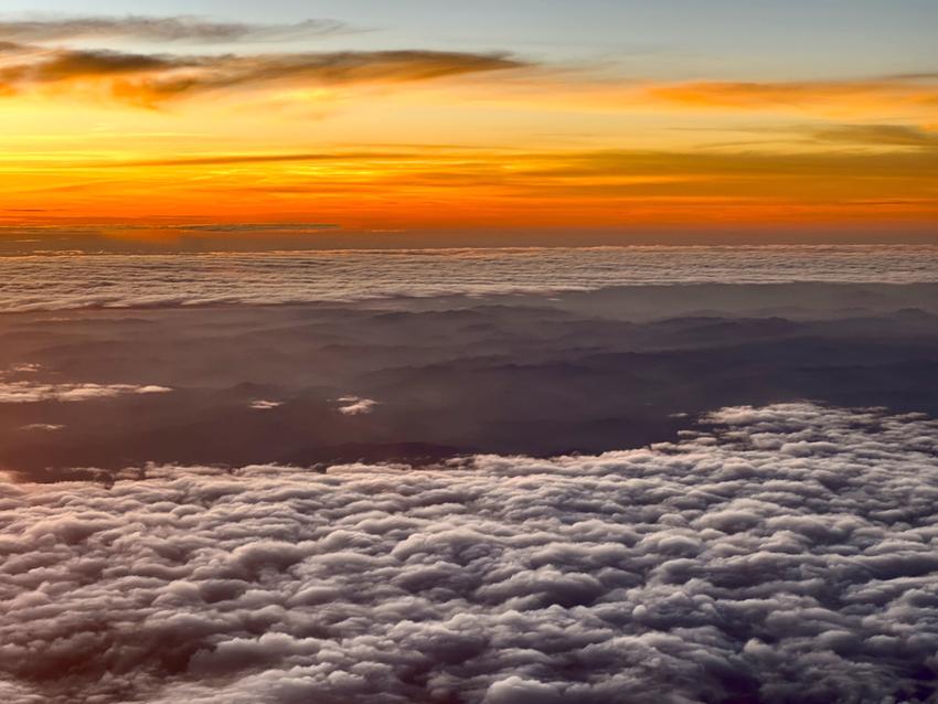 A view from an airplane with a sea of cloud and mountains below it at sunset