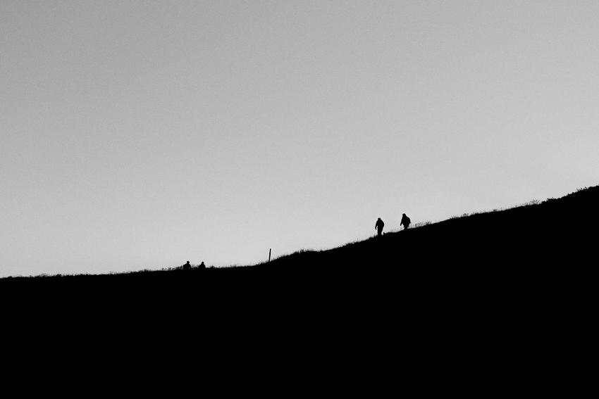 A black & white silhouettes of hikers on a mountain ridge